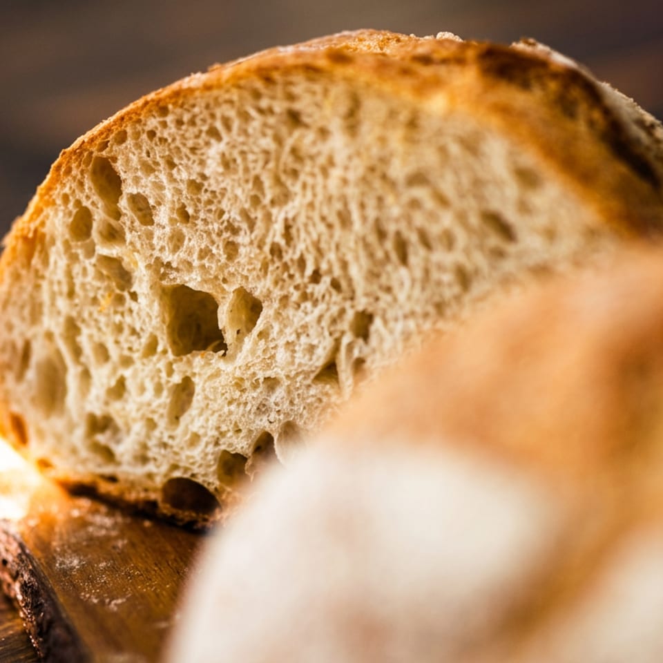 Close-up of a sliced loaf of rustic bread with a porous texture on a wooden surface.