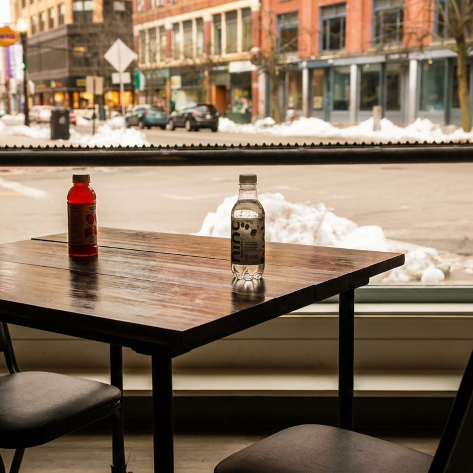 A table with two drinks and chairs, looking out a window at a snowy city street.